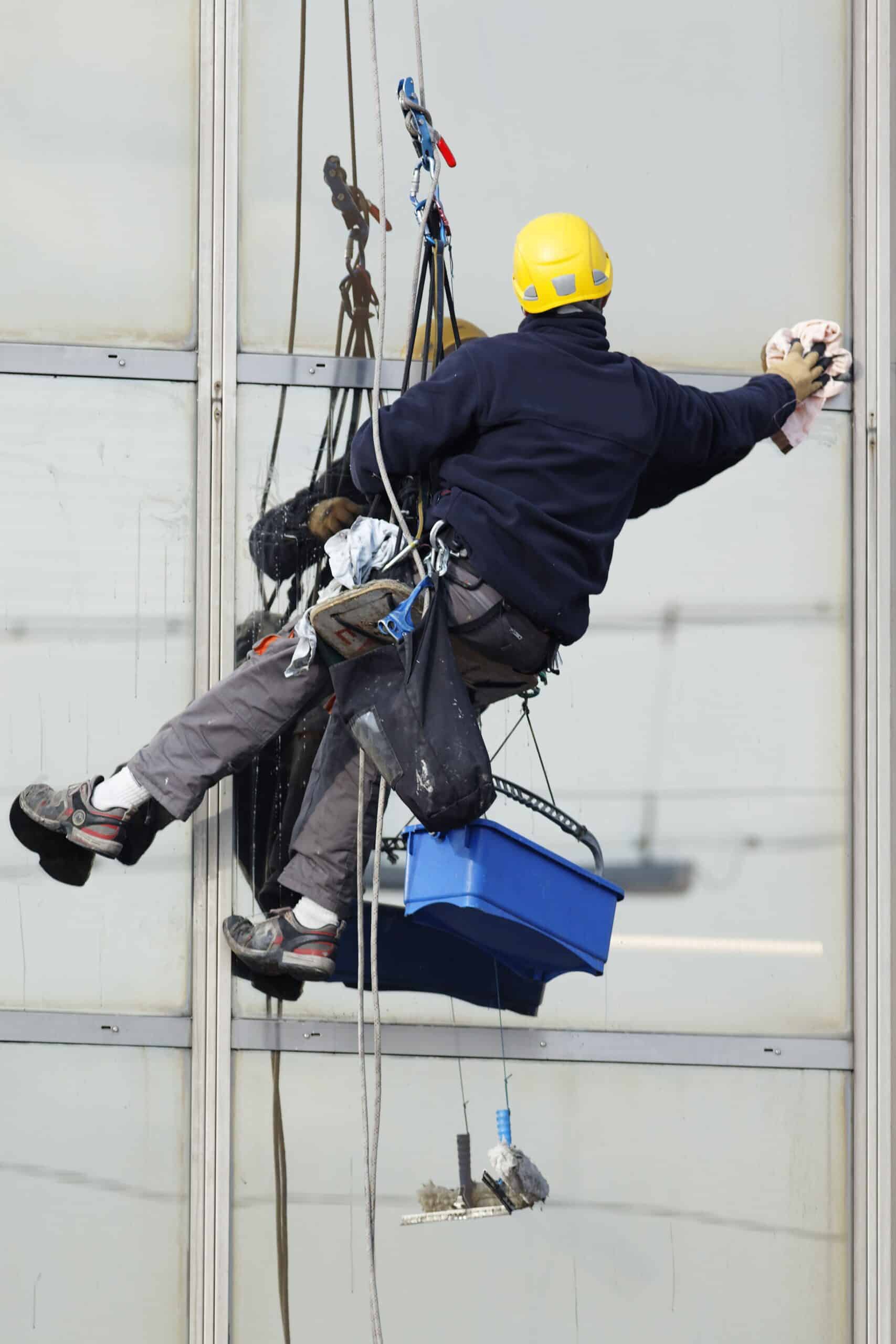 Glazenwasser met valbeveiliging die op hoogte ramen wast