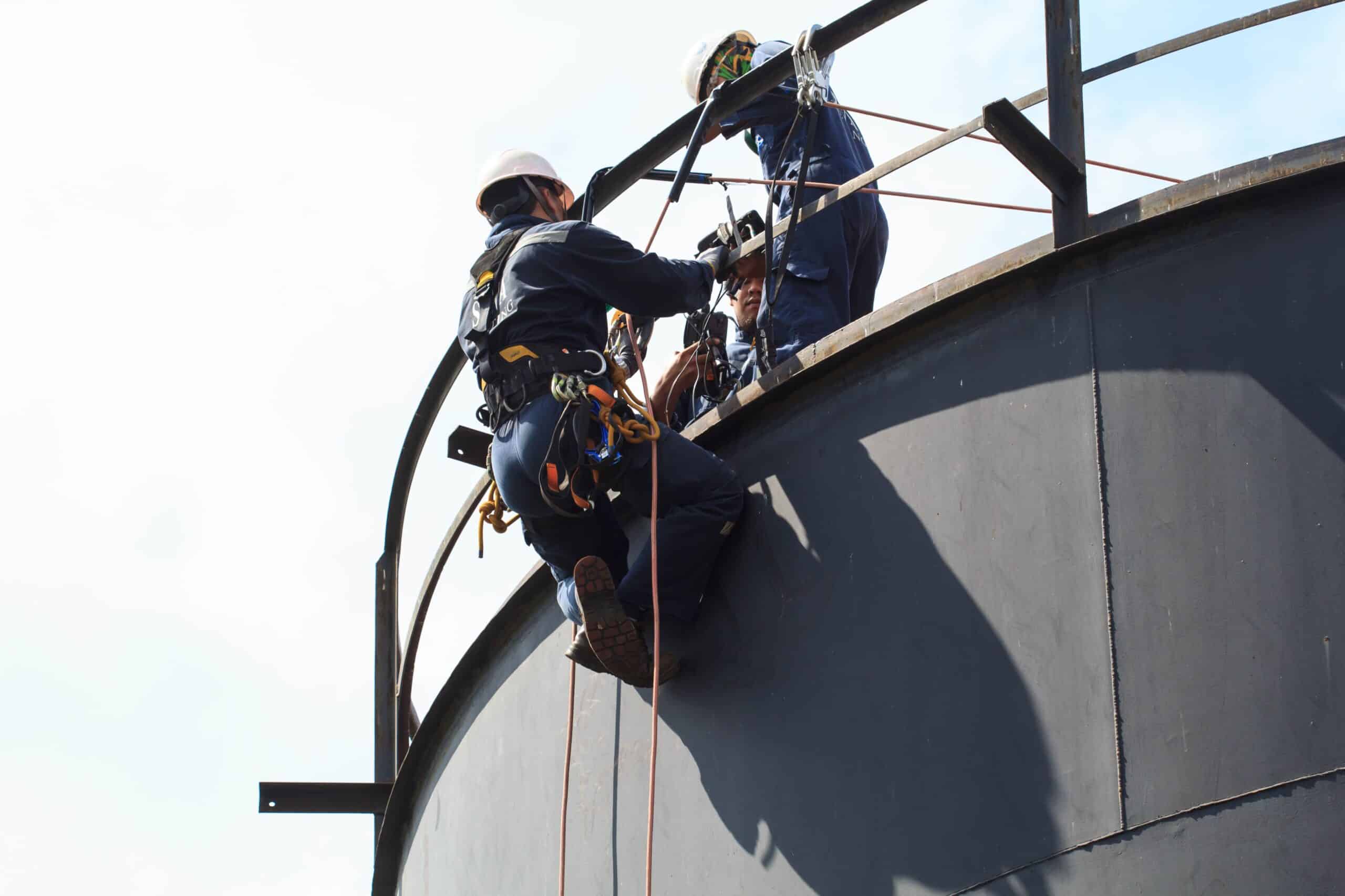 achteraanzicht van twee monteurs met valbeveiliging op hoogte in een industriële omgeving